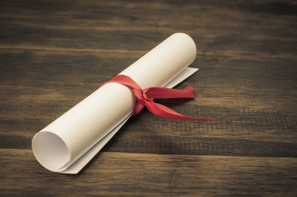 A parchment diploma scroll, rolled up with red ribbon on wooden backgroung
